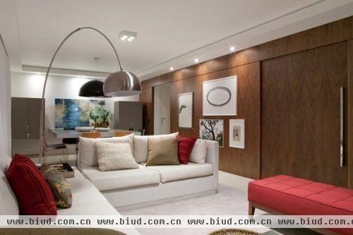 现代简洁的公寓却十分精致且充满时尚感。整面墙的胡桃木饰面是客餐厅区域最主要的装饰面，其余没有太多的装饰，白色的墙面和窗帘，白色布艺沙发与地毯依旧迎合整体空间的舒适和清爽，配合黑色、红色、灰色调的家具配饰更显时尚精致。