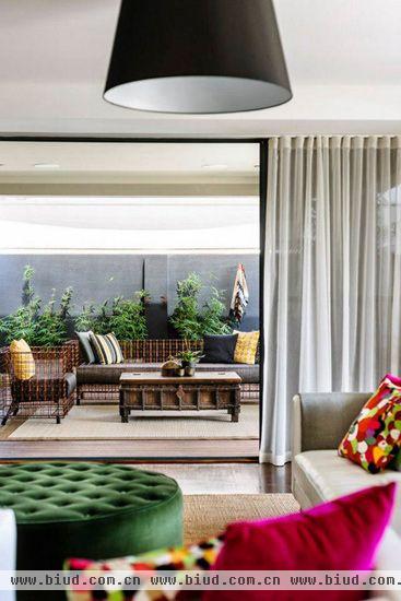 桃红色的抱枕和深绿色的桌子的撞色搭配很有视觉冲击，也很好地活跃了客厅氛围。用玻璃门来区分客厅和室外休息区，让两厅在视觉上既相连又有所区别，同时保证了室内有充足的采光。