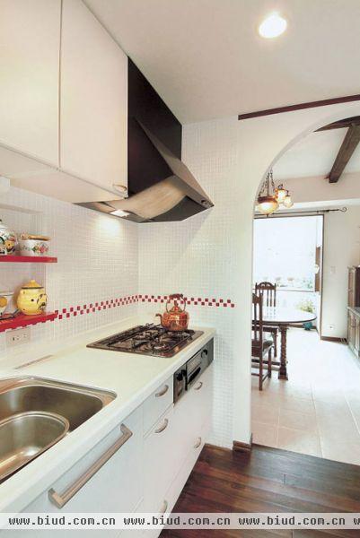  家庭装修样板房：厨房就在饭厅的另一侧。采用明亮的白色做主颜色，墙上贴上红色的小方砖，简洁大方而又不显单调。 