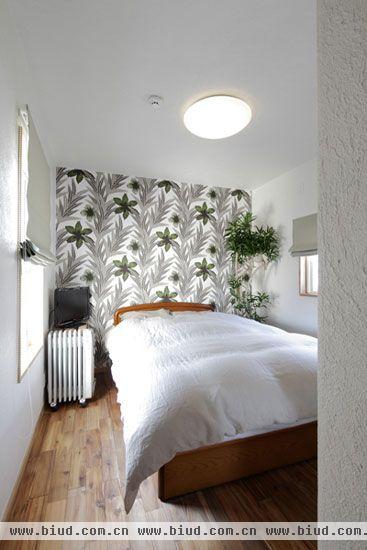 卧室区域，木质的床搭配白色的床品，淳朴的日式风情吹满整个空间。绿色花朵样式的壁纸装饰整个床头部分，再搭配床头的绿叶植物，浓郁的自然之风让整个卧室区域都变得格外清爽自然。白色卷帘式的窗帘，选择性的将光线投入屋内，简洁实用。
