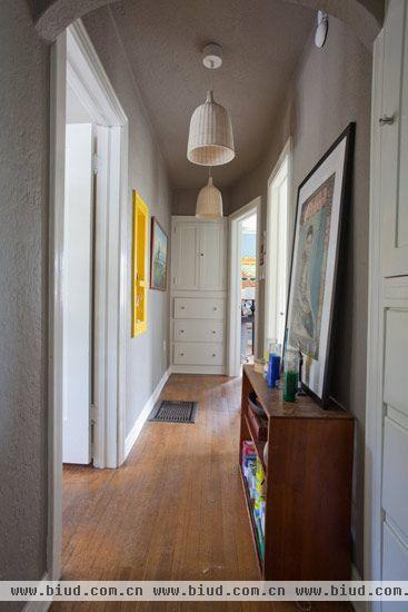 回到用餐空间的另一扇门，是一条朴素的走廊连接着两个卧室以及卫生间。木地板以及一旁的地柜，搭配上时尚的藤制吊灯，让空间从一而终地贯彻着这种朴实里面流露出来的时尚。