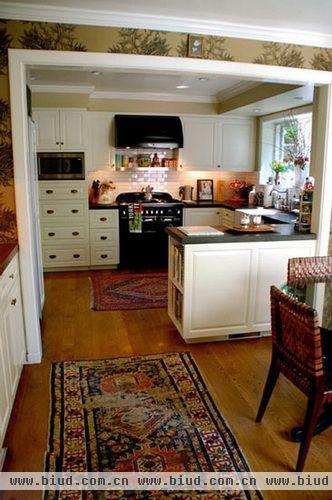 厨房采用半开放设计，虽然采用白色橱柜，但仍旧一展浓郁风情，深黄色的地板配合艳丽的民族风情地毯，让厨房也变得极具风情，窗台摆放的一盆银柳，充斥着生活气息。
