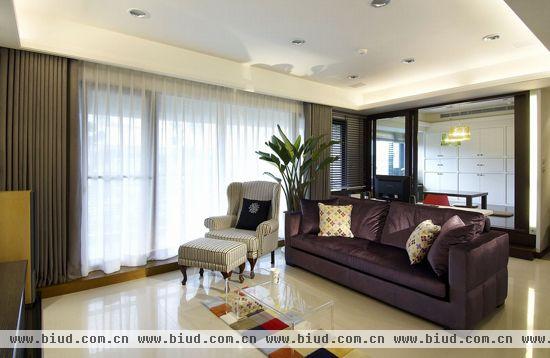 客厅延揽大片落地窗光线，完全符合“窗明几净”的氛围，深紫色丝绒沙发、透明茶几、欧风主人椅及皮制脚凳，透过家具配置诠释出独特时尚感，同时保留了公共空间的敞朗。