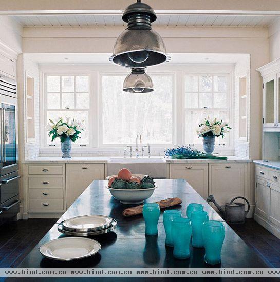 大面积的窗户让厨房空间宽敞明亮，白色橱柜发挥收纳功能，并与窗户保持统一的风格，让厨房整体更融洽。内嵌式电器为厨房腾出更多可用空间，置于厨房中间的黑色吧台方便了食物和厨房用具的摆放。