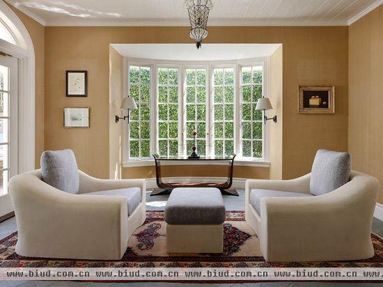 窗口位置增加了窗台空间用以物品的收纳与展示。大面积的木框窗户不但保证客厅有充足的采光，而且让空间看起来更加干净整洁。复古的地毯和对称摆放的沙发固定了客厅区域，与浅棕色背景墙自然融合。
