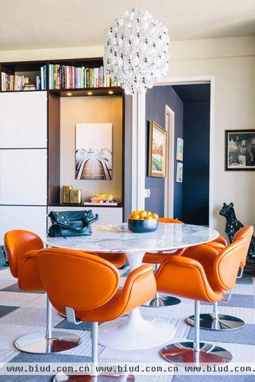 餐厅设计时尚感和金属感十足，选用橙色的餐椅配上蓝色的餐碗与内墙，用色大胆创新。华美的吊灯、金属感的小狗摆设和各种壁画的搭配也为餐厅增色不少。