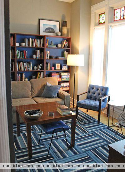 进到客厅，用蓝色的软装、白色的墙壁为主题，保持客厅的明亮清爽。不同深浅蓝色构成的竖纹地毯，斑驳的蓝色井然有序地排列，体现不同层次的蓝色。在蓝色的软装世界中，加入灰色的沙发，调和蓝色的压迫感。