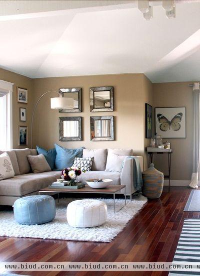 灰白色的L型大沙发搭配浅蓝色的抱枕，冷暖色调平衡而且让蓝色首先映入人的眼球，和茶几前的蓝白单人沙发相映衬。浅棕色墙面的加入增加了秋天的气息，和白色天花板的搭配室内的明亮开阔。墙壁上的壁画有序而保持距离的摆放是保持室内整齐的秘诀。