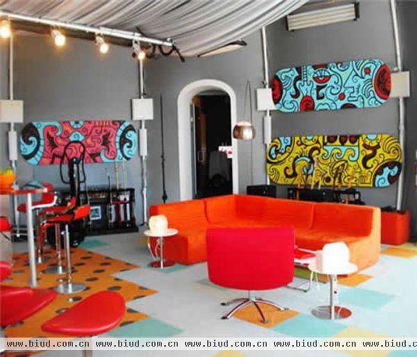 这个客厅空间中摆放着一张橘红色的沙发和几张红色的座椅，使得整个空间一下子活力四射，墙面上椭圆形的彩色抽象画板装点墙面，颜色上与沙发的颜色相协调。