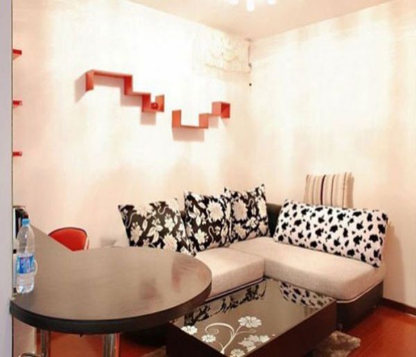 客厅以白色为主色调，白色现代风格的沙发、黑白图案的抱枕、镜面的花朵图案茶几，都使这个空间散发着现代简约风格的特点。墙面上橙色的置物架和地板色调相统一。