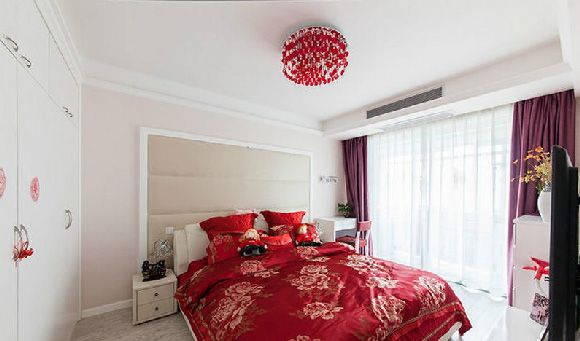 卧室床头背景墙为淡粉色，墙面上做了浅咖色的软包，简单精致的设计，喜庆的红色床品和灯具，让空间更具有温暖气息。
