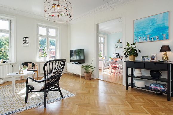 客厅的白色墙面与天花板都漆上白色，搭配温润的木质地板，就是最基本的简约风格。客厅的鸟笼吊灯，放上几只鲜艳的小鸟，让人有种置身丛林的错觉。而在采光良好的厨房，漆上粉蓝色的墙面，白色的餐桌，混搭粉色及红色的餐椅，让用餐空间多了分活泼的氛围。来看看瑞典这间马卡龙风公寓吧！