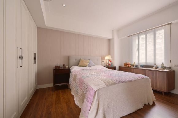 这间卧室床头背景墙整个以偶粉色竖条纹的硬包装饰而成，加上一面墙整个大窗设计，从而显得空间通透明亮。