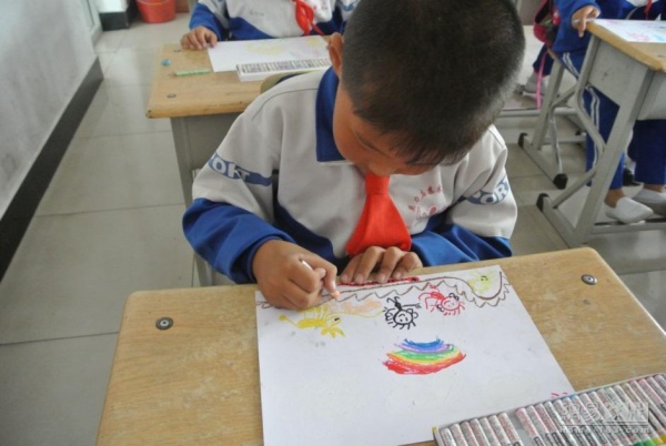 图为一位小朋友拿到志愿者带来的画笔后，在图纸上描绘自己心中的美好